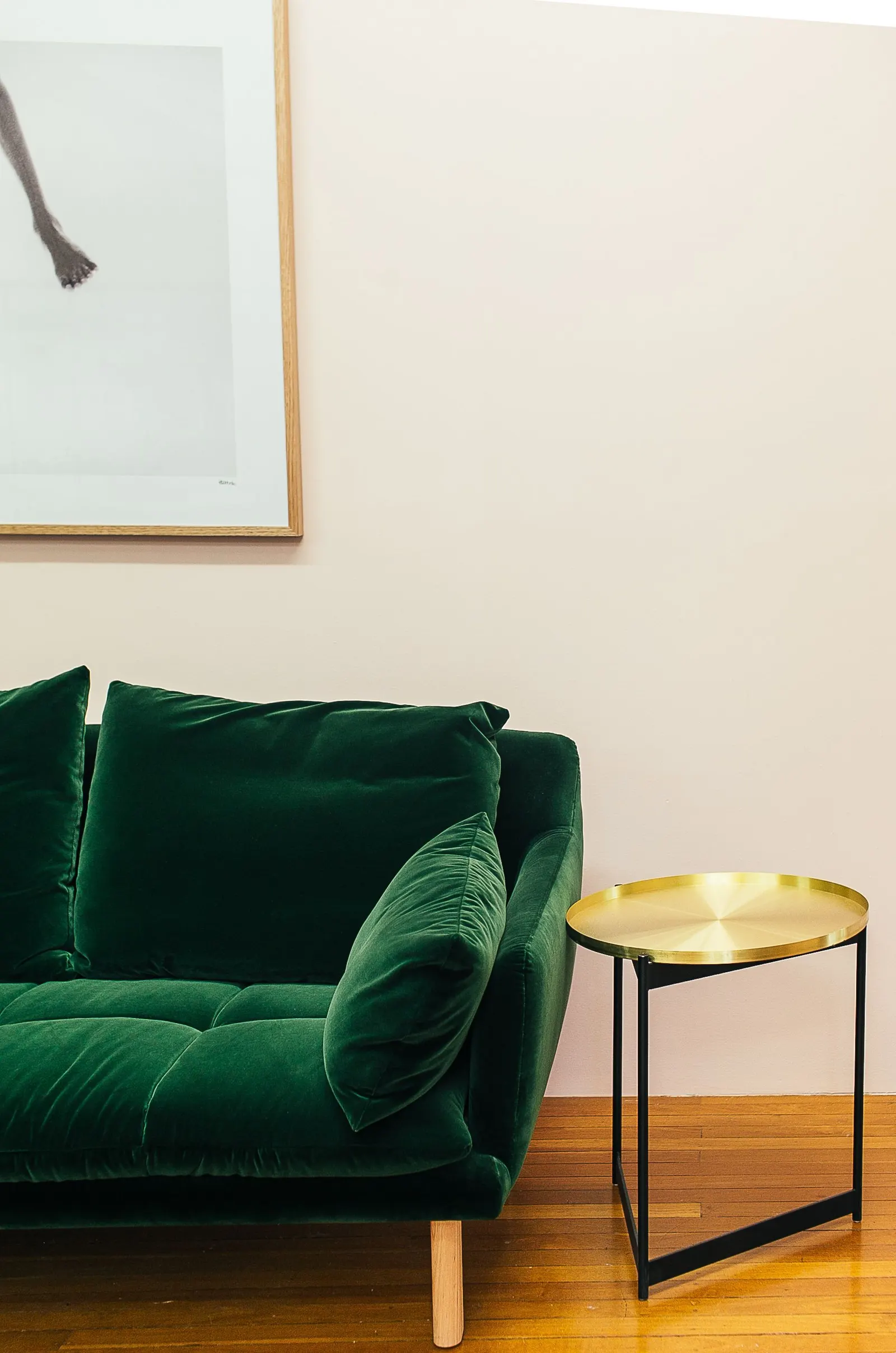 Sofá de terciopelo verde esmeralda y mesa auxiliar de latón sobre suelo de madera